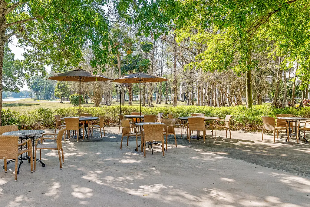 An exterior view of 3 tables with 11 chairs and two umbrellas outside of  a 55+ apartment senior living community